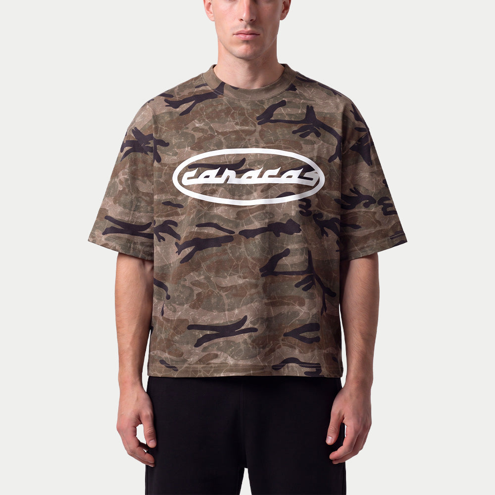 Hombre llevando la camiseta boxy de camuflaje verde «Caracas» de Caracas Merch con el óvalo blanco
